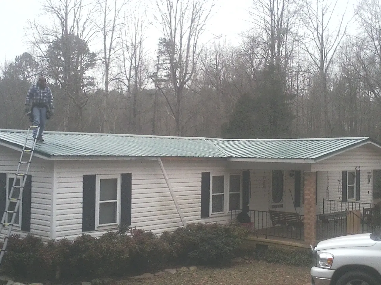 Worker on a ladder beside a new green metal roof on a ranch home in Chesnee