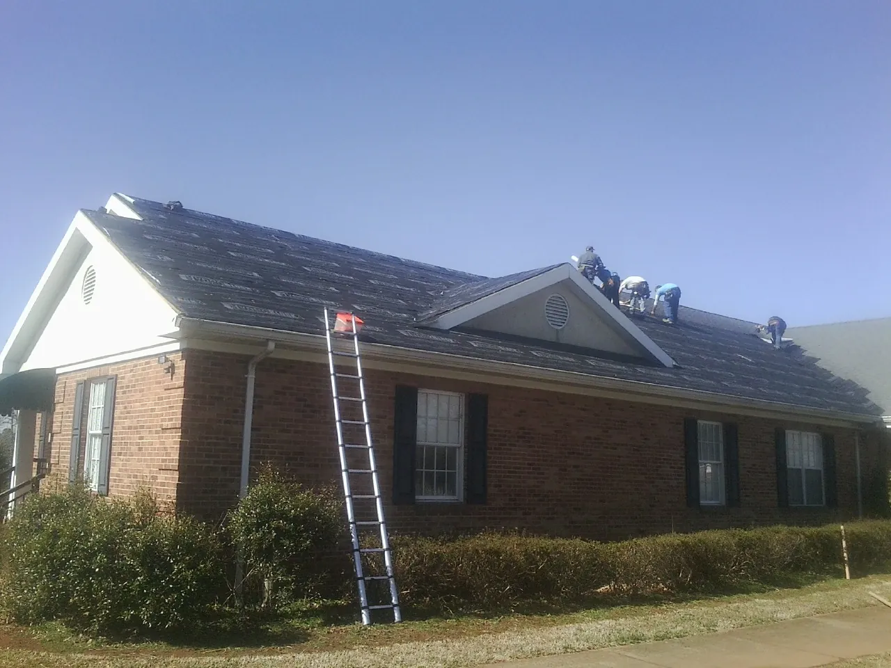 Crew tearing shingles off a brick ranch roof with a ladder set — Metal Roof Repair work by our crew in Chesnee