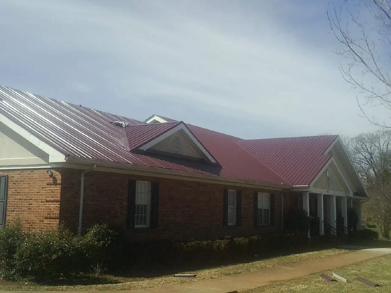 Red metal roof with gabled entries on a long brick building, from a Hail Damage Roof Repair job in Chesnee