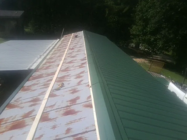 Old rusted panels beside newly installed green metal roofing — Wind Damage Roof Repair by Roofing Brothers in Chesnee