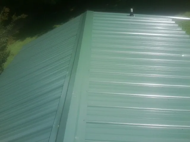 New green metal panels meeting at the ridge of a roof — Flat Roof Repair work by our crew in Chesnee