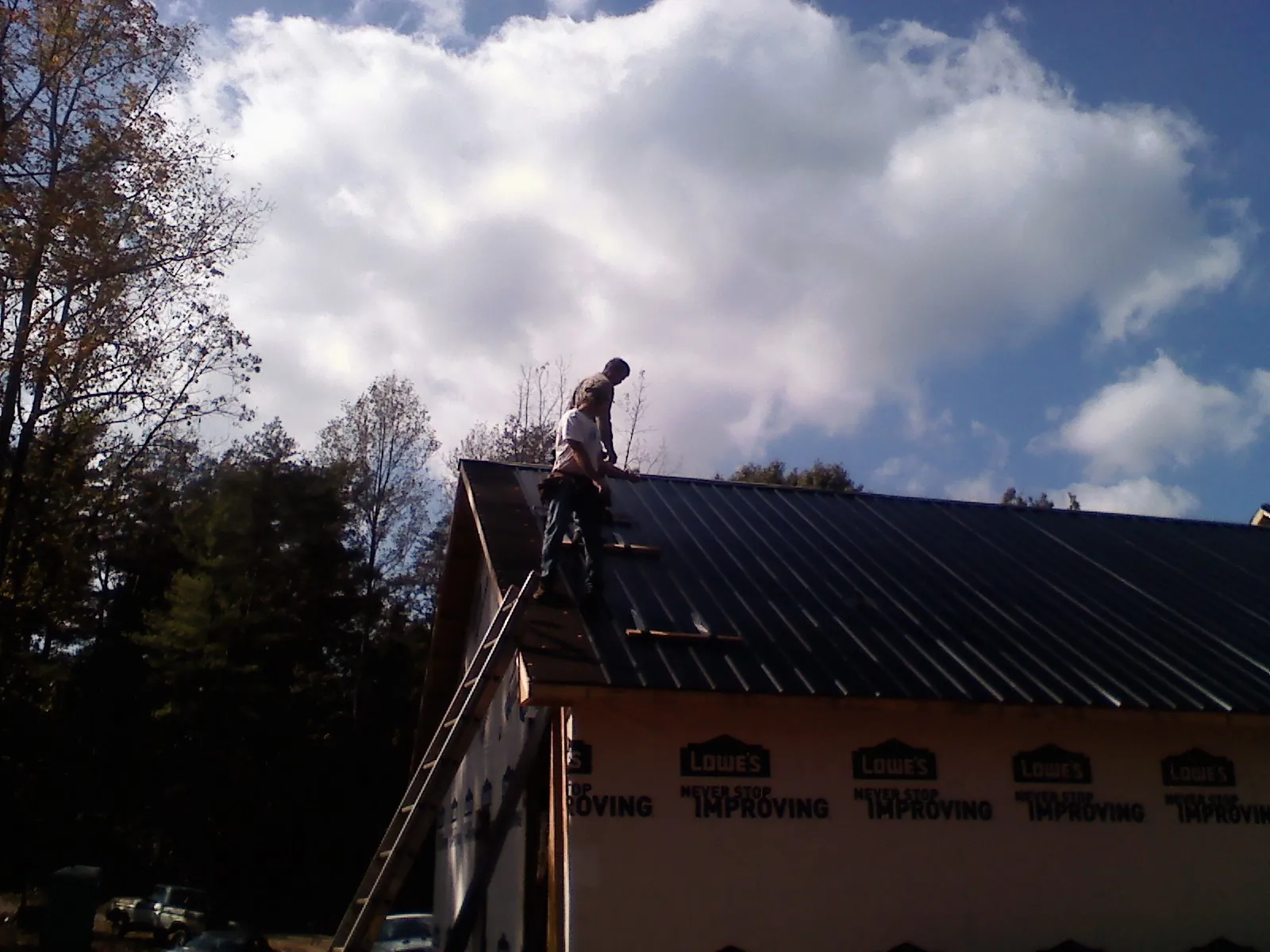Roofer fastening dark metal panels high against a cloudy sky, from a Roof Inspection job in Chesnee